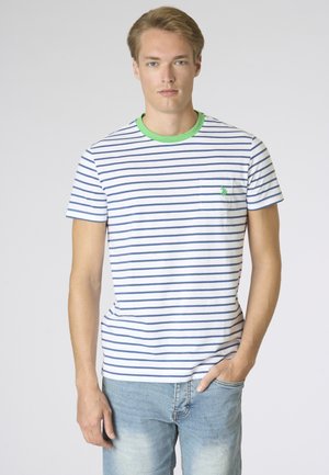 Giovane uomo con capelli biondi indossa una maglietta bianca con righe orizzontali blu navy e colletto verde, abbinata a jeans chiari.