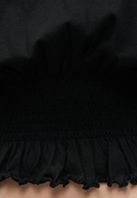 Μαύρο ύφασμα με ελαστική μέση που συγκεντρώνεται και λεπτομέρεια με βολάν στο τελείωμα.