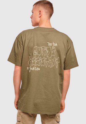 Olivengrøn oversized t-shirt med grafisk tekstdesign i hvid på bagsiden, korte ærmer og en løs pasform.