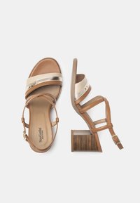 Braune und cremefarbene Sandalen mit Absätzen, metallischen Akzenten, verstellbarem Knöchelriemen und strukturiertem braunem Blockabsatz. Aus glattem Leder und synthetischen Materialien.