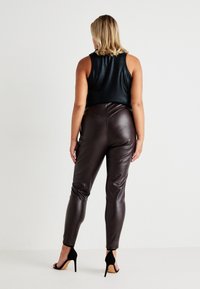 Black sleeveless top with a shiny finish, paired with brown faux leather skinny pants. Black high-heeled sandals complete the look.