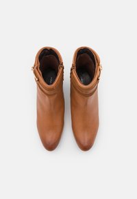 Botas de tobillo de cuero marrón con una textura suave, punta afilada y una correa decorativa con detalle de metal en el tobillo.