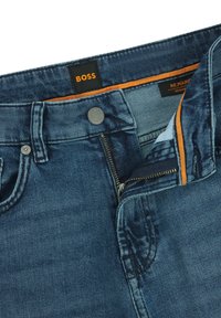 Denim jeans with a regular fit, dark blue color, visible stitching, a metal button, and zipper fly. Grey lining with orange accents.