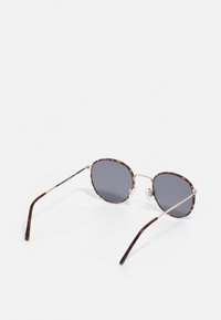 Gafas de sol redondas con un patrón de carey y acentos dorados. Las lentes grises y las almohadillas nasales transparentes mejoran la comodidad. Montura de metal, patillas delgadas.