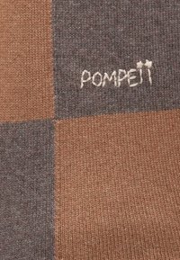 Pleteno platno s uzorkom smeđih i sivih kvadrata te mekanom teksturom. Izvezeni logo "POMPEIT" u svijetlo bež koncu.