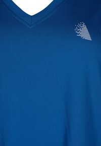 Niebieski t-shirt z dekoltem w serek, wykonany z gładkiej tkaniny; na górnej lewej stronie znajduje się teksturowane białe logo; minimalistyczny design.