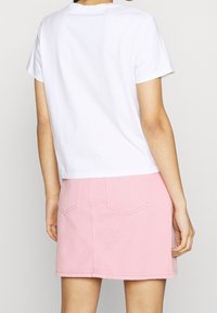 Vit bomull T-shirt med kort ärm, kombinerad med en rosa denim minikjol som har två bakfickor och synlig sömnad.