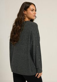 Maglione grigio lavorato a maglia con una vestibilità rilassata, caratterizzato da sottili accenti decorativi sulle maniche. Tessuto morbido e maniche lunghe.