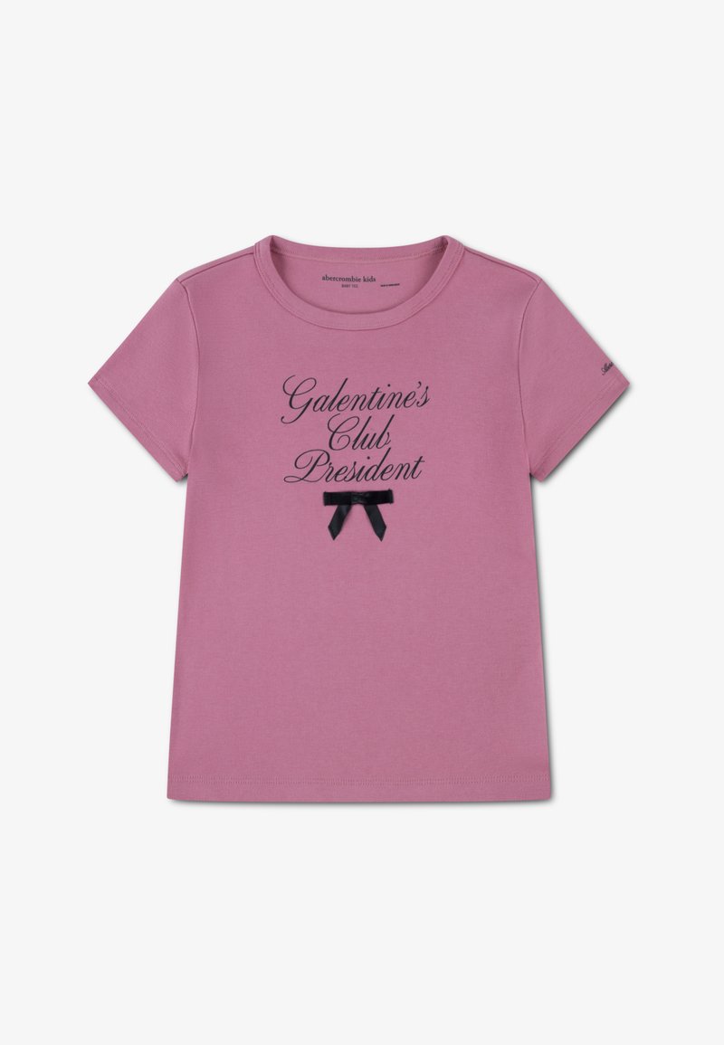 Ροζ κοντομάνικο t-shirt με μαύρο τυπωμένο κείμενο "Πρόεδρος Λέσχης Γκαλέντιν" και μια μικρή μαύρη λεπτομέρεια φιόγκου κάτω από το κείμενο.