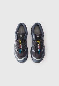 Pilnas pilkų ir mėlynų Salomon bėgimo batelių su greito raiščio sistema ir spalvingomis ženklelių etiketėmis ant balto fono.