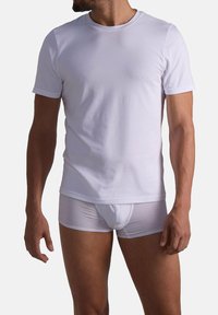 Torso maschile che indossa una semplice t-shirt bianca a maniche corte e boxer bianchi su uno sfondo neutro.