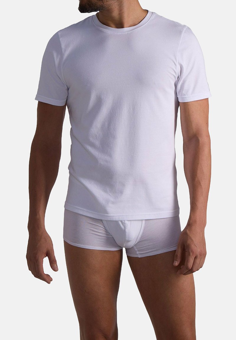 Torso maschile che indossa una semplice t-shirt bianca a maniche corte e boxer bianchi su uno sfondo neutro.