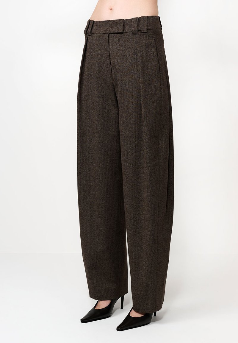 Barna, magas derekú nadrág, texturált anyagból készült, plisszírozott elülső részével, övbujtókkal és széles szárú fazonnal. Fekete hegyes sarkú cipővel párosítva.