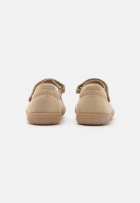 Zapatos de ante color arena con un perfil bajo y una correa trasera, que presentan una suela texturizada y el logo de la marca embellecido en el talón.