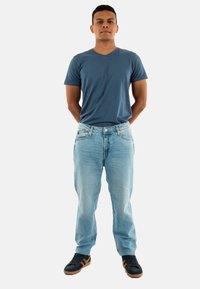 Camiseta de cuello en V azul, jeans de mezclilla claros y zapatillas negras con acentos marrones. Jeans de corte recto con un ligero desgaste y sin patrones visibles.