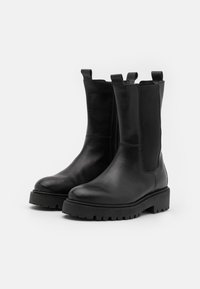 Botas de cuero negro hasta el tobillo con paneles laterales elásticos, punta redondeada y suela de goma gruesa con un patrón de tracción.