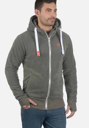 Grijze fleece hoodie met rits, witte trekkoorden, zijzakken en rood merkembleem. Zachte textuur en getailleerd ontwerp.