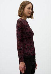 Bordeaux ribbel langekous top met een zwart bloemenpatroon. Ronde hals, aansluitend ontwerp en soepele textuur. Gemaakt met zwarte broek.