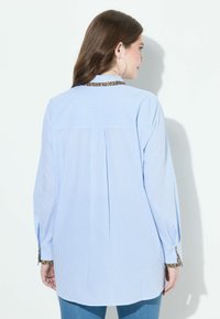 Camicia a righe blu chiaro con maniche lunghe, con un'accoppiatura in stampa leopardata sul colletto e sui polsini. Vestibilità comoda e tessuto morbido.