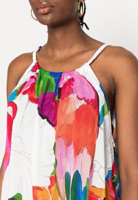 Vícebarevný květinový top z lehkého materiálu, se volným střihem, tenkými ramínky a živým vzorem růžové, modré a zelené barvy.