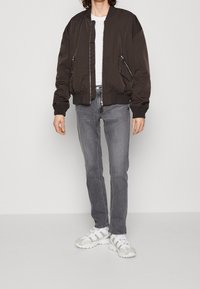 Svart bomberjacka med dragkedjefickor, vit t-shirt, grå jeans och vita sportiga sneakers med texturerad detalj.