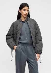 Γκρι μπουφάν bomber με ραμμένο σχέδιο και κουμπιά με πάτημα, διαθέτει ελαστικές μανσέτες και κορδόνια, συνδυασμένο με αντίστοιχο γκρι πουκάμισο με κουμπιά και παντελόνι.