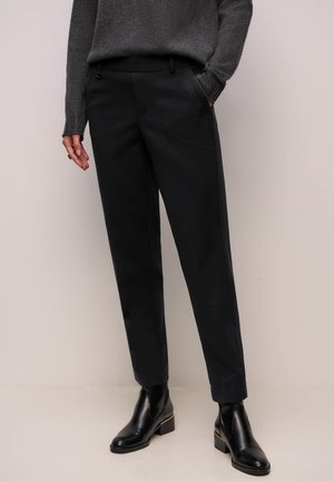 Persona che indossa pantaloni aderenti neri con tasche laterali, maglione a maniche lunghe grigio scuro e stivaletti neri con tacco a blocco.