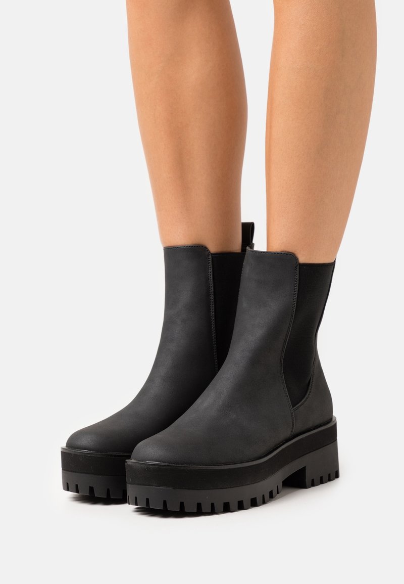 Botas negras hasta el tobillo con un acabado de cuero suave, paneles laterales elásticos, punteras redondeadas y suelas gruesas de goma texturizada.