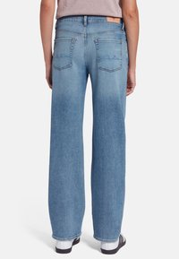 Jeans in denim blu chiaro con gambe larghe, vita alta e delicate cuciture nelle tasche posteriori. Il cinturino ha un dettaglio in pelle tan.