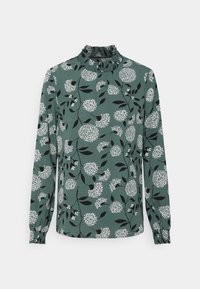 Grön blommig blus med långa ärmar, med en volangkrage, vita blommönster och svarta blad på ett texturerat tyg.