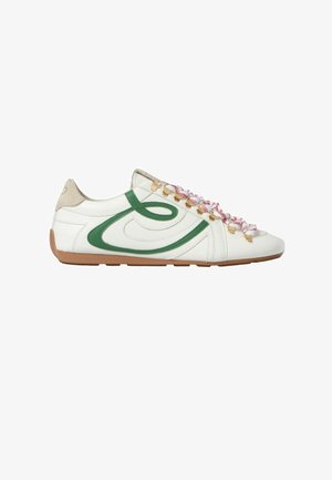 Baskets basses blanches avec une bande incurvée verte, un patch talon beige, des lacets rayés rouge et blanc, et une semelle marron, vues de profil.