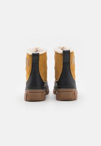 Brune suedeboots og svarte skinnankler med kunstpelsfôring og gummisåle, med en merket bakdel og et elegant design.