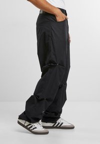 Zwarte, losse broek met geplooide delen en drukknoopdetails. Gemaakt van lichtgewicht stof, met zijzakken en een rechte pasvorm.
