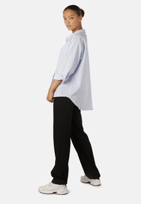 Camicetta oversize azzurro chiaro con maniche arrotolate, abbinata a pantaloni neri e sneakers bianche. Presenta una sola tasca sul petto e un orlo arrotondato.