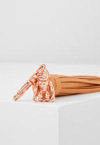 Rose gold metal keychain featuring a monkey figure attached to a tan rubber strap with a smooth texture and subtle branding detail.