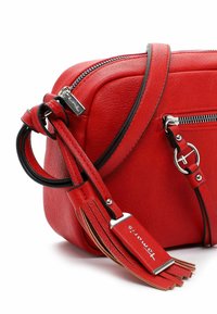 Rød læder crossbody taske med sorte kanter, sølv lynlås, rund metalring og kvastmærke prægede med "Tamaris" på hvid baggrund.