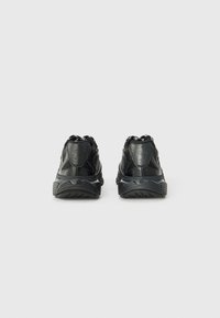 Chaussures de sport noires avec panneaux en mesh, soutien rembourré à la cheville et semelle en caoutchouc texturée. Elles disposent d'un talon renforcé et de lacets contrastants.