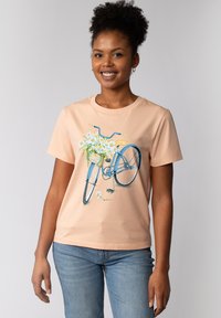 Perzikkleurig katoenen T-shirt met een blauwe fietsafbeelding en witte madeliefjes in het voorwielmandje. Korte mouwen en een ronde hals.