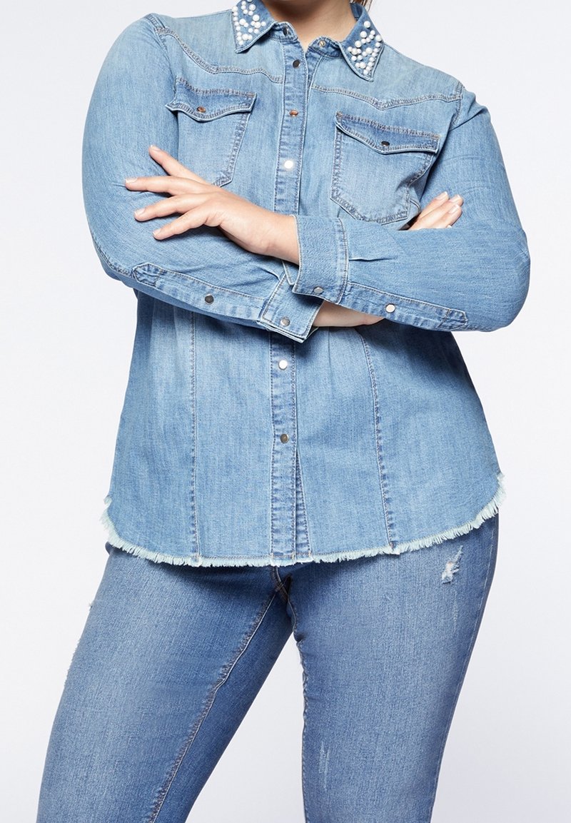 Ljusblå denimskjorta med utsmyckad krage, knäppning framtill och två bröstfickor. Fransad nederkant vid botten.