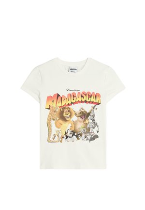 T-shirt bianca in cotone con una grafica colorata "Madagascar" che presenta animali da cartone animato tra cui una giraffa, un leone, una zebra e pinguini.