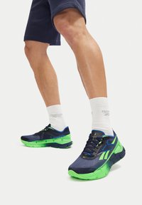 Scarpe sportive da uomo con tomaia blu navy, dettagli verdi, rete traspirante, suola testurizzata e lacci a contrasto. Adatte per attività sportive.