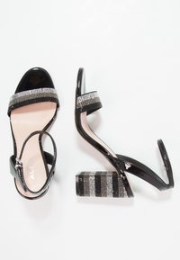 Svarta lackläder högklackade sandaler med en strassprydd rem och en blockklack med ett randigt mönster av glänsande detaljer.