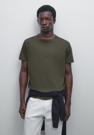 Oliven grøn kortærmet T-shirt lavet af bomuld, med en rund halsudskæring og en afslappet pasform. Mørkeblå sweater bundet om livet.