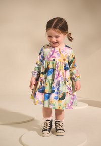 Meerlaagse jurk met lange mouwen, bloemenpatronen en elastische manchetten; gecombineerd met zwarte hoge sneakers en kant sokken.