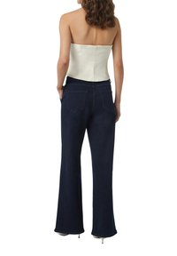 Biały top bez ramiączek, ciemnoniebieskie dzwony z kieszeniami, z dodatkowymi akcentami na bocznych szwach i gładką teksturą. Widok z tyłu pokazuje dopasowanie topu i szczegóły spodni.