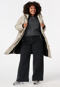 Doudoune beige, sweat gris avec des motifs de cœurs, jean large noir avec des accents de boutons et baskets grises.