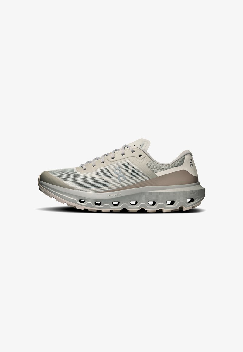 Chaussure de sport beige clair et grise avec semelle perforée, empeigne en mesh, lacets et logo de marque sur le côté et le talon.