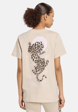 Kvinde iført beige t-shirt med stort leopard silhuetprint på ryggen og matchende beige bukser, vist bagfra.