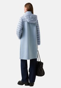 Světle modrá péřová bunda s měkkým povrchem, se kapucí, dlouhými rukávy a rovný střih. V kombinaci s tmavými džíny a černou kabelkou.
