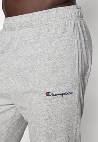 Graue Fleece-Jogginghosen mit einem elastischen Bund, seitlichen Taschen und besticktem "Champion"-Logo in Marineblau und Rot am unteren Bein.